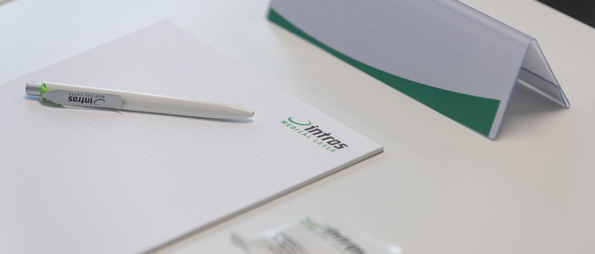Briefbögen, Namenschilder und ein Kugelschreiber mit dem Logo des Firma intros auf einem Schreibtisch