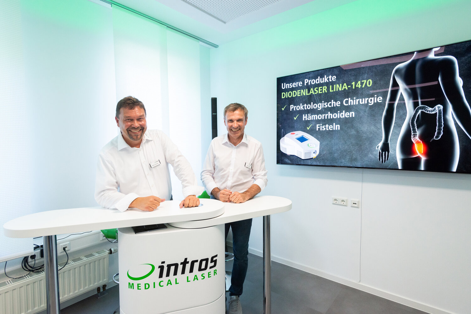 Rainer Sauerbier und Elmar Hahne, Geschäftsführer bei intros Medical Laser an einem Stehpult vor einem Poster
