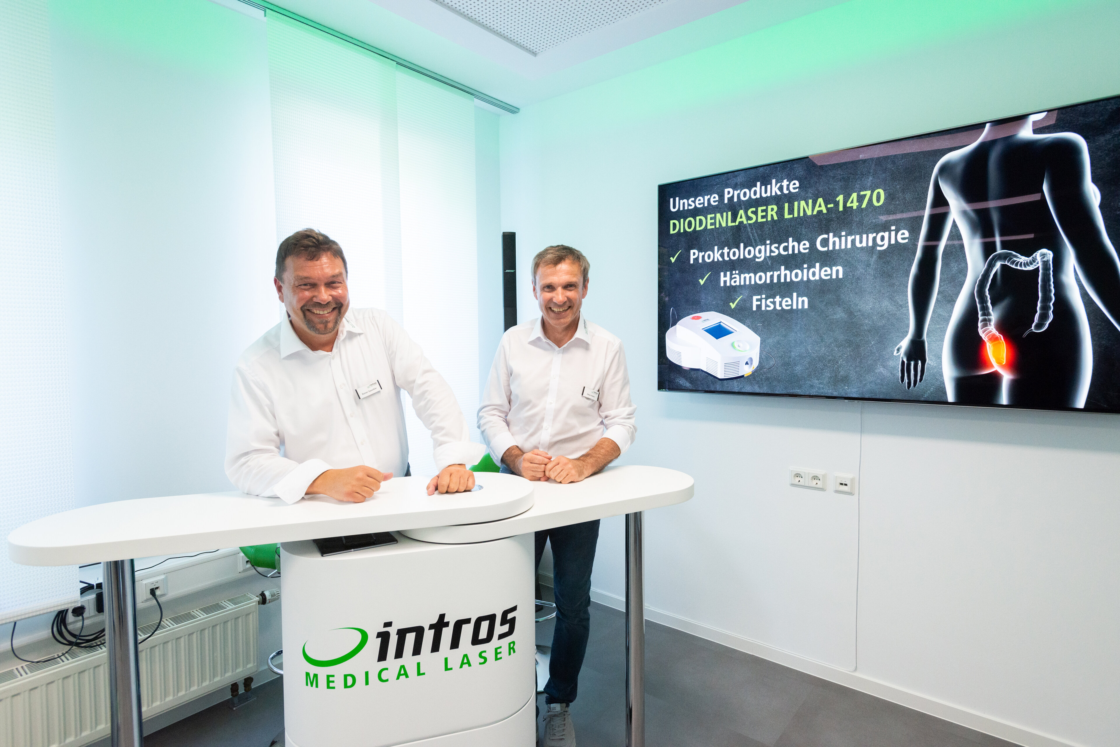 Rainer Sauerbier und Elmar Hahne, Geschäftsführer bei intros Medical Laser an einem Stehpult vor einem Poster