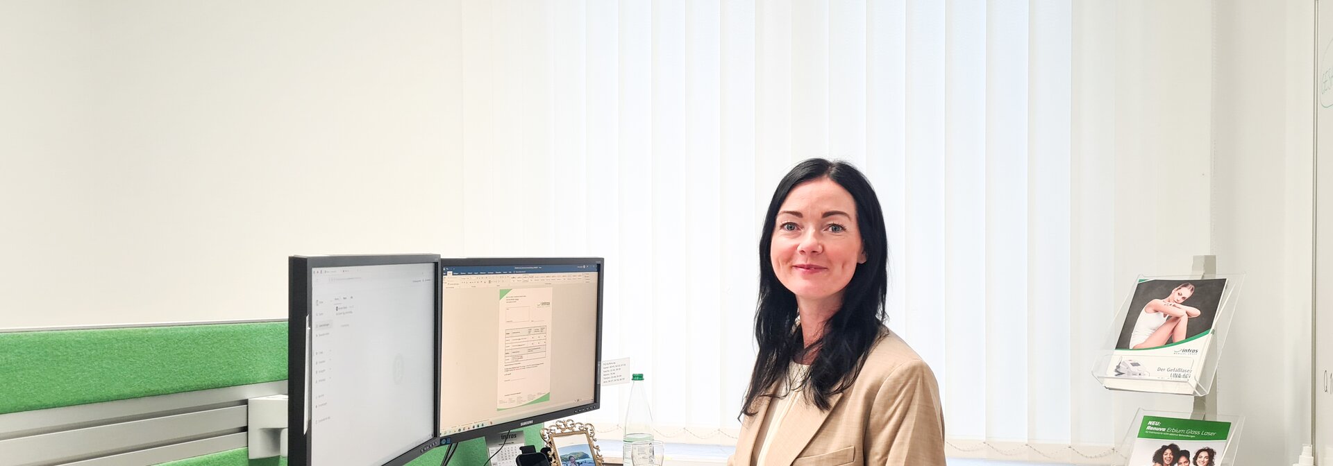 Mitarbeiterin von intros Medical Laser an seinem Schreibtisch, sie lächelt freundlich in die Kamera