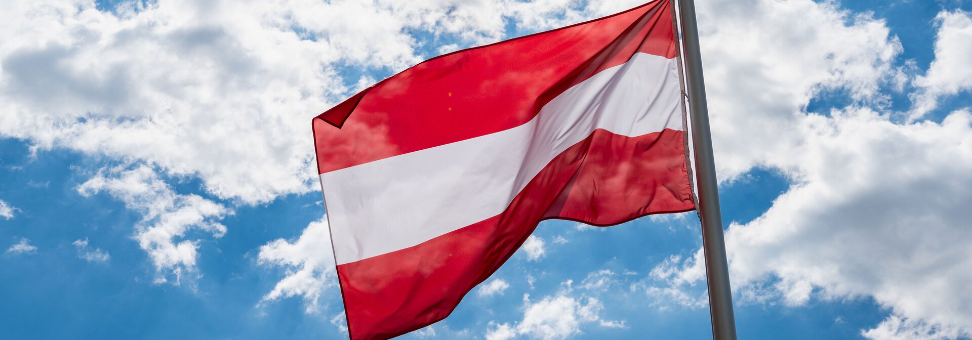 Flagge Österreichs vor blauem Himmel mit leichten Wolken